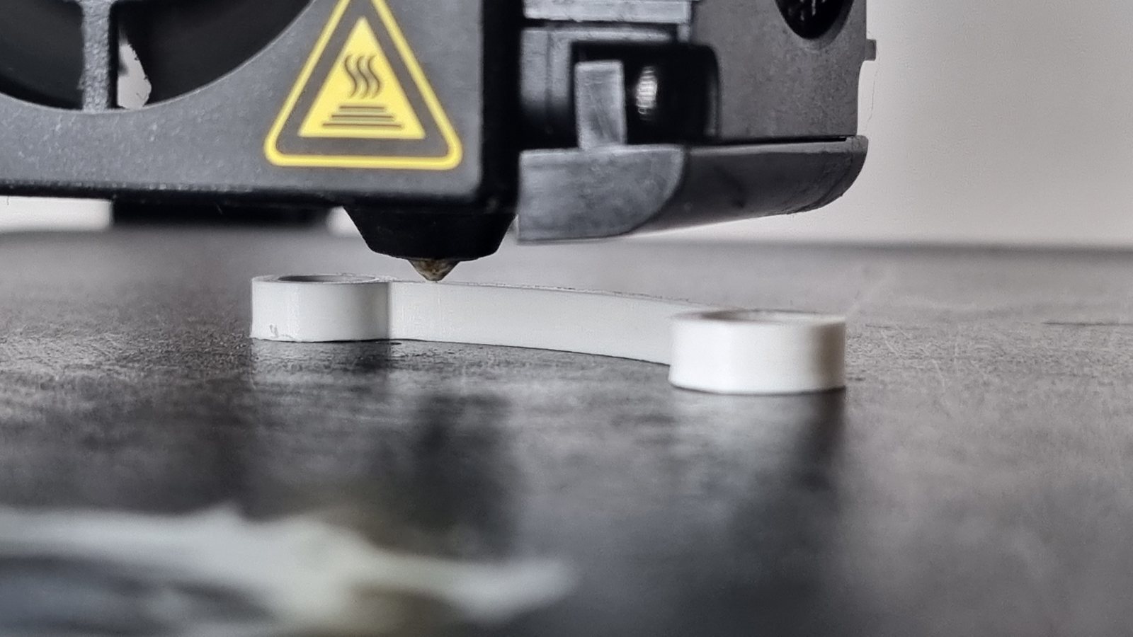 Gros plan de la buse d'une imprimante 3D en train de déposer le plastique blanc qui forme la pièce de remplacement.